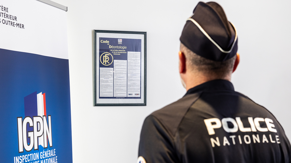 Policier de dos devant un kakémono IGPN et la charte de déontologie 